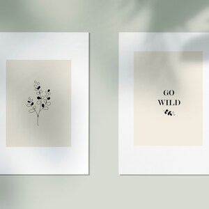May include: Two minimalist prints with white frames. The print on the left features a simple line drawing of a sprig of leaves. The print on the right features the text "GO WILD" with a small sprig of leaves below.