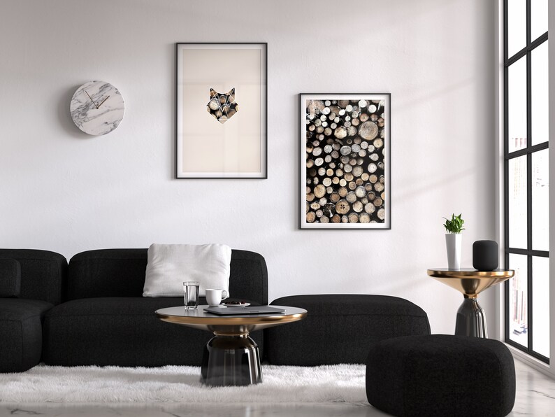 May include: A black sectional sofa with a white pillow sits in front of a white wall with two framed prints. One print features a geometric wolf design, and the other features a stack of wooden logs. A round marble clock hangs on the wall. A black and gold coffee table sits in front of the sofa. A small black ottoman sits in front of the coffee table. A small black side table with a gold top sits next to a window. A small potted plant sits on the side table.