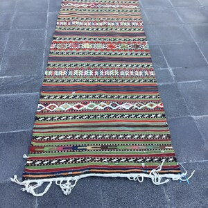 May include: A rectangular, handwoven rug with a vibrant, striped pattern. The rug features bands of red, green, blue, and brown, interspersed with geometric designs. White fringe accents the ends. This rug is suitable for a hallway or entryway.