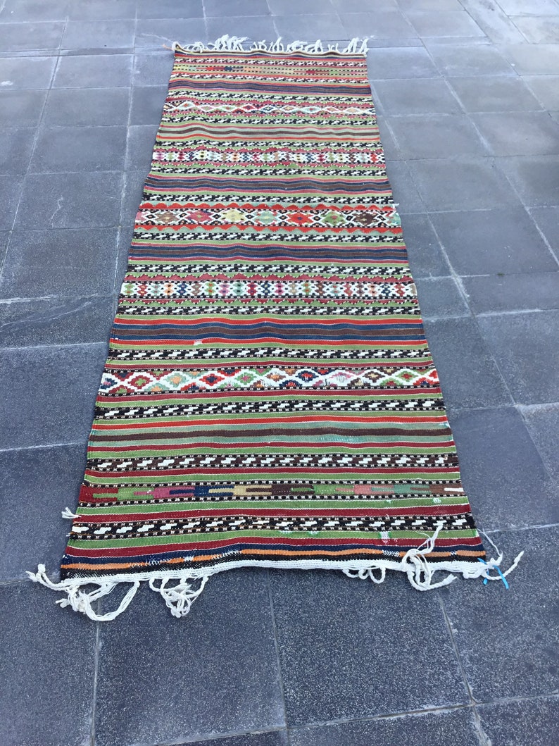 May include: A rectangular, handwoven rug with a vibrant, striped pattern. The rug features bands of red, green, blue, and brown, interspersed with geometric designs. White fringe accents the ends. This rug is suitable for a hallway or entryway.