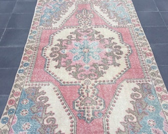 May include: A vintage Turkish rug with a pink, beige, and blue floral pattern. The rug has a distressed look and is made of wool.
