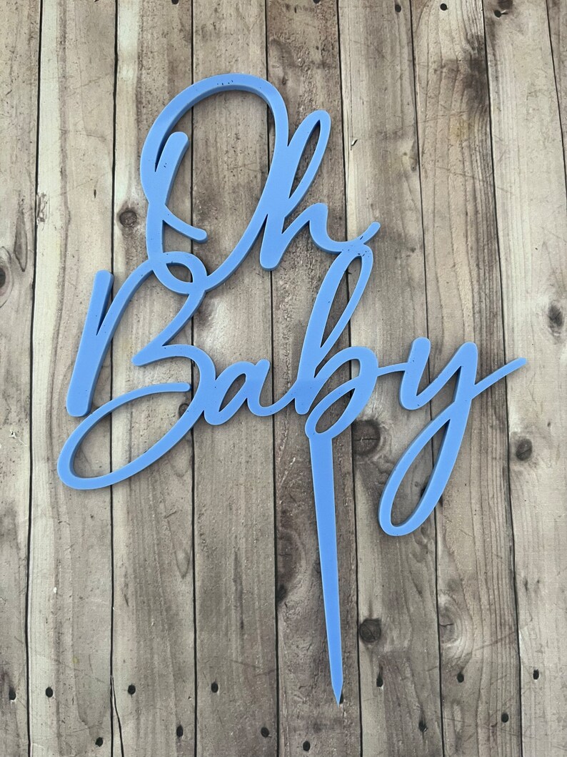 May include: A light blue cake topper with the words "Oh Baby" in a cursive font.