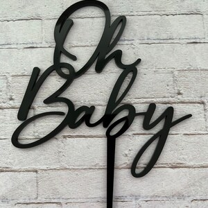 May include: Black acrylic cake topper with the words "Oh Baby" in a cursive font.