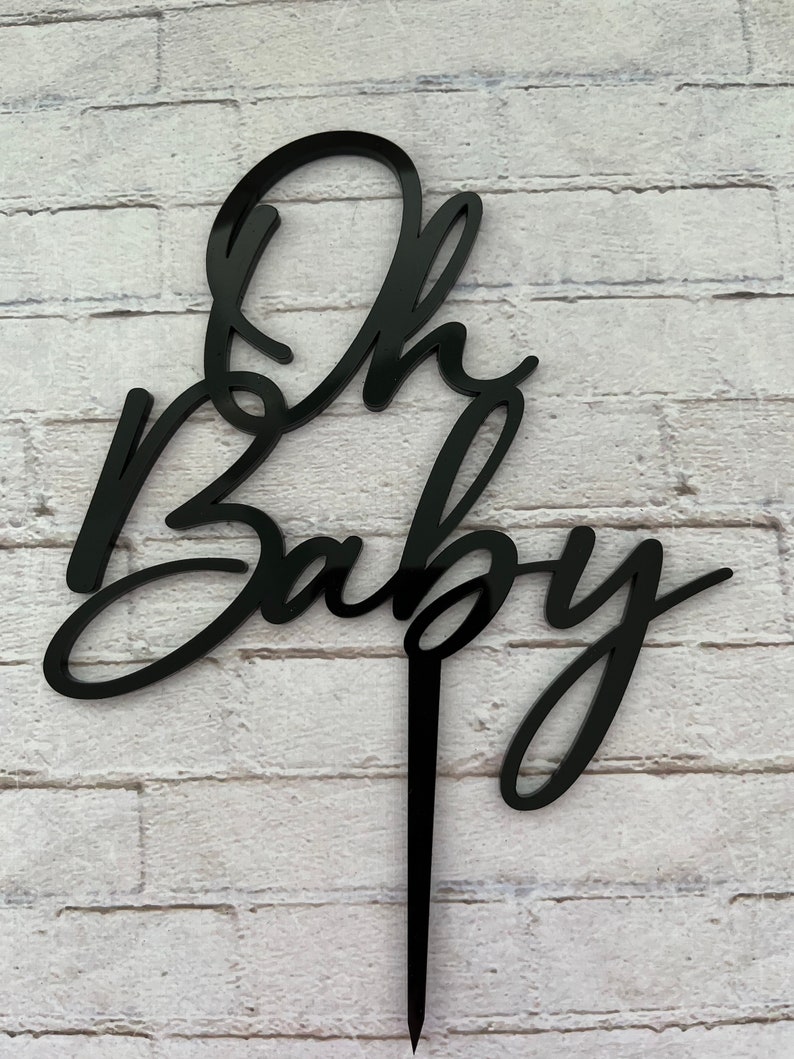 May include: Black acrylic cake topper with the words "Oh Baby" in a cursive font.