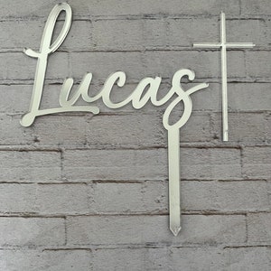 May include: Silver mirror-like acrylic name sign with the name "Lucas" in cursive script and a silver cross.