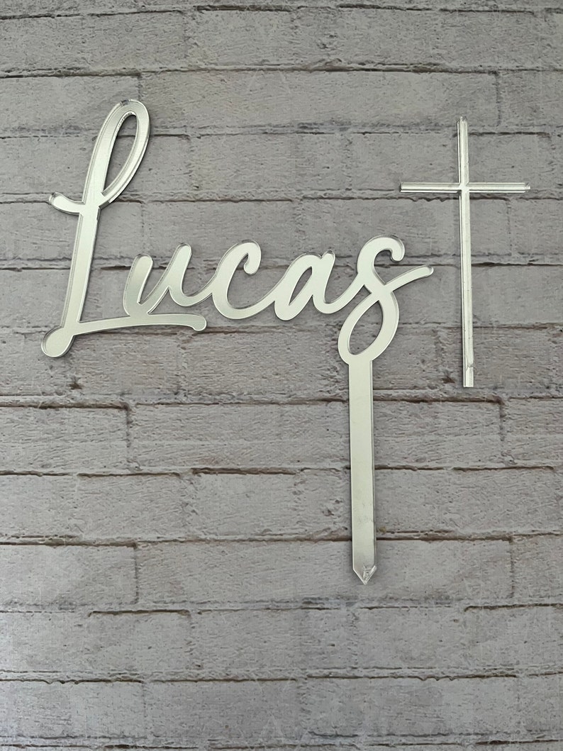 May include: Silver mirror-like acrylic name sign with the name "Lucas" in cursive script and a silver cross.