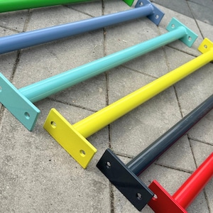 Może przedstawiać: Zbliżenie na kilka kolorowych metalowych wsporników półek. Wsporniki są pomalowane w odcieniach zieleni, niebieskiego, turkusu, żółtego, szarego i czerwonego. Każdy wspornik ma prostokątną płytę montażową z dwoma otworami i cylindrycznym ramieniem.