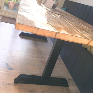 May include: A rustic wooden table with a natural finish and black metal legs. The table is made of reclaimed wood and has a unique character. The legs are sturdy and provide support for the table.