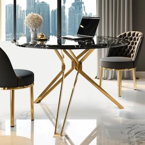 Op de afbeelding: Een moderne eethoek met een ronde zwarte marmeren tafel met goudkleurige metalen poten. Twee zwart beklede stoelen met gouden accenten omringen de tafel. Een laptop staat op de tafel, met uitzicht op de stad door het raam.