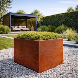 Könnte beinhalten: Ein großer, quadratischer, rostfarbener Pflanzkübel, gefüllt mit grünem Laub. Der Pflanzkübel steht auf einem Bett aus kleinen, weißen Kieselsteinen in einer Gartenanlage. Im Hintergrund sind eine moderne Pergola und ein gepflegter Rasen zu sehen.