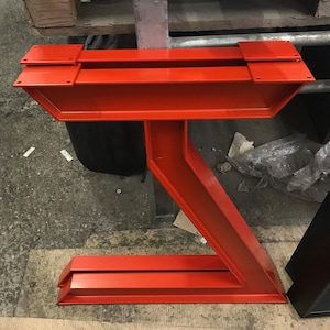 May include: A pair of bright red metal table legs with a unique Z-shaped design. The legs are made of sturdy metal and have a smooth, painted finish.