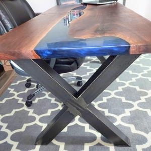 May include: A wooden desk with a blue epoxy river running through the centre. The desk has a black metal X-shaped base.