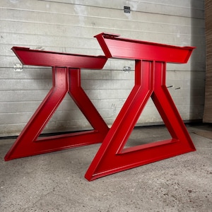Puede incluir: Dos patas de mesa de metal rojo con una base triangular y una parte superior rectangular. Las patas están hechas de metal grueso y tienen un acabado liso y pintado.