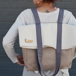 Op de afbeelding: Een grote, tweekleurige tote bag met een witte bovenkant en een bruine onderkant. De tas heeft twee lange, grijze banden en een klein gouden logo met de tekst "boozy" aan de voorkant.