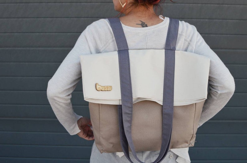 Op de afbeelding: Een grote, tweekleurige tote bag met een witte bovenkant en een bruine onderkant. De tas heeft twee lange, grijze banden en een klein gouden logo met de tekst "boozy" aan de voorkant.