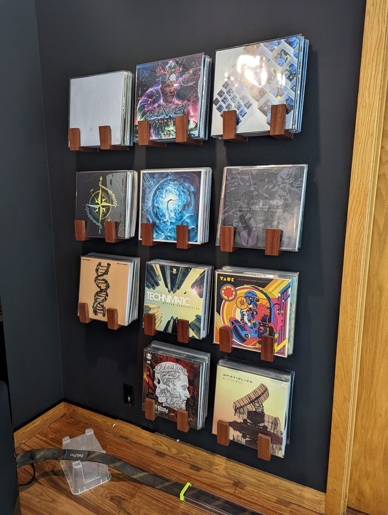 x9 sets of vinyl wall holders in mahogany wood mounted on a black wall, each holding around 15 vinyls.