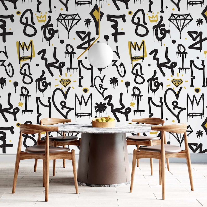May include: A dining room with a round, marble-top table and four wooden chairs. The walls are covered in a white wallpaper with a black and gold graffiti pattern featuring crowns, diamonds, hearts, and stars.