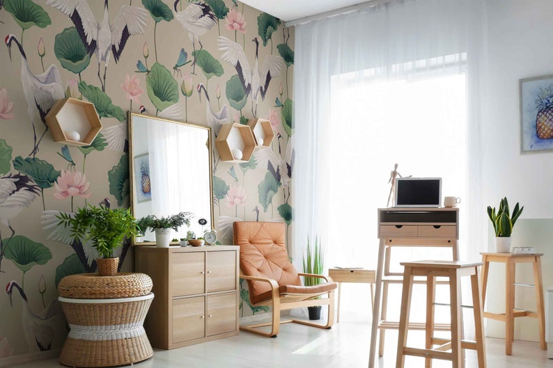 May include: A home office with a light brown standing desk, a laptop computer, and a brown leather chair. The wall is decorated with a wallpaper featuring white cranes, pink lotus flowers, and green leaves.