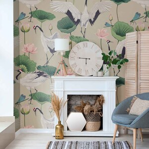 May include: A white fireplace mantel with a white clock on top. The clock has roman numerals and black hands. The fireplace has a brick interior and a white surround. There is a blue armchair with a beige pillow in front of the fireplace. The wall behind the fireplace has a wallpaper with a green and pink floral pattern and white cranes.
