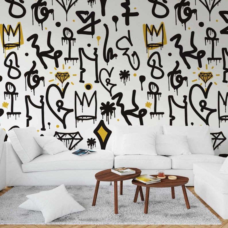 May include: A white couch with two brown coffee tables in front of it. The wall behind the couch is covered in a black and gold graffiti pattern with hearts, crowns, diamonds, and other abstract shapes.