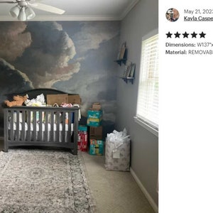 May include: A nursery room with a removable wallpaper mural depicting a cloudy sky. The wallpaper is 137 inches wide by 110 inches tall, or 350 cm by 280 cm. A crib is in the center of the room, with a white dresser to the left and a window to the right.