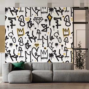May include: A white wall with a black and gold graffiti pattern. The pattern includes crowns, diamonds, and abstract shapes. A gray couch is in front of the wall.