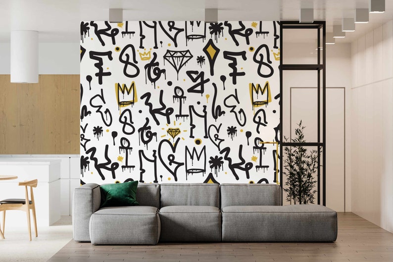 May include: A white wall with a black and gold graffiti pattern. The pattern includes crowns, diamonds, and abstract shapes. A gray couch is in front of the wall.