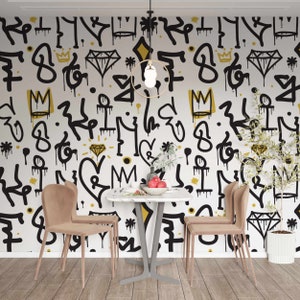 May include: A dining room with a white wall featuring a black and gold graffiti pattern. The room has a square table with three chairs and a potted plant.