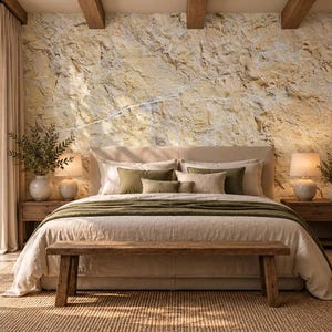 May include: A bedroom featuring a large bed with a beige duvet and olive green pillows, positioned against a textured stone wall mural. A wooden bench sits at the foot of the bed, flanked by two wooden nightstands with lamps and vases.