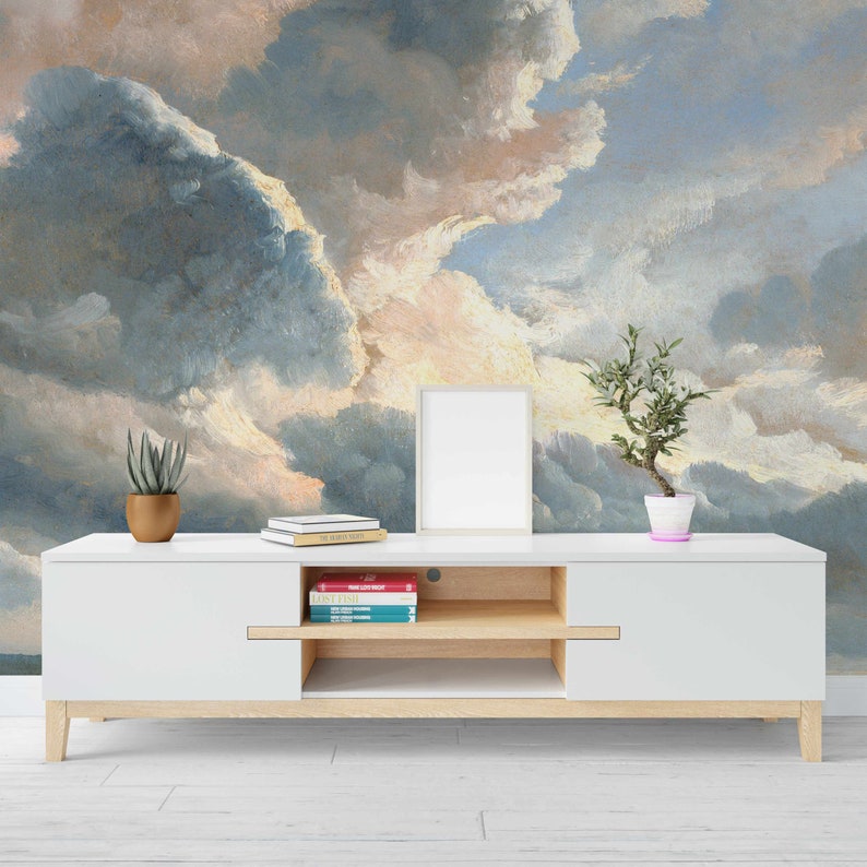 May include: A white entertainment center with two shelves and a white frame picture on top. The entertainment center is in front of a wall with a painting of a cloudy sky.
