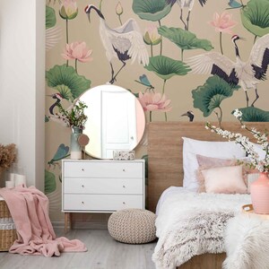 May include: A bedroom with a white dresser, a bed with a white fluffy blanket and a pink throw pillow, a round mirror, a woven ottoman, and a wall mural featuring cranes, lotus flowers, and dragonflies.