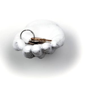 May include: A white, hand-shaped wall-mounted key holder. The sculpture holds a set of keys on a metal ring. The fingers and palm are detailed with a textured finish. The keys are a mix of silver and bronze.