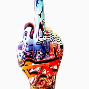 May include: A hand sculpture with the middle finger extended, covered in vibrant graffiti art. The artwork features a mix of colors including red, blue, orange, and white, with intricate patterns and designs. The background is plain white.