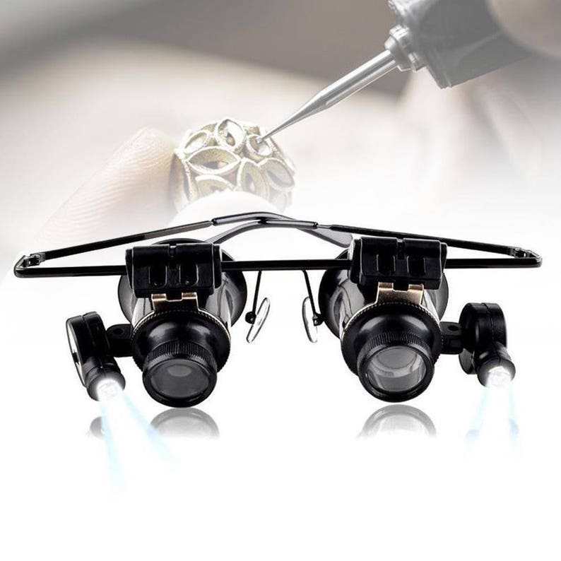 K&ouml;nnte beinhalten: Schwarze Lupenbrille mit eingebauten LED-Lichtern, die f&uuml;r den freih&auml;ndigen Gebrauch konzipiert ist. Die Brille hat ein Kopfband und verstellbare Linsen.