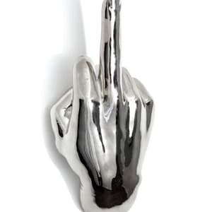 May include: A silver-colored sculpture of a hand giving the middle finger, set against a white background. The sculpture has a reflective, metallic finish, with detailed finger and hand features.
