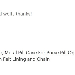 May include: A silver metal pill container with a black and white floral design. It has a chain attached and is a stash pendant with felt lining.