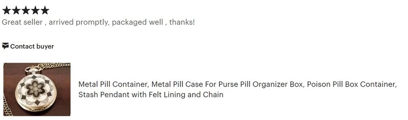 May include: A silver metal pill container with a black and white floral design. It has a chain attached and is a stash pendant with felt lining.