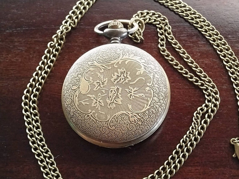May include: A gold pocket watch with a chain. The watch face has an intricate floral design.