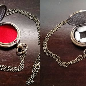 May include: A gold-toned necklace with a round locket pendant. The locket is open and has a red velvet interior. The locket is also shown open with four white pills inside.