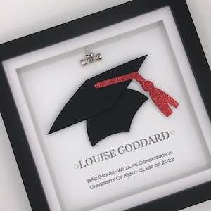 May include: A framed graduation keepsake featuring a black graduation cap and red tassel. The name "LOUISE GODDARD" is printed below the cap, along with the text "BSC (HONS) - WILDLIFE CONSERVATION UNIVERSITY OF KENT - CLASS OF 2023".