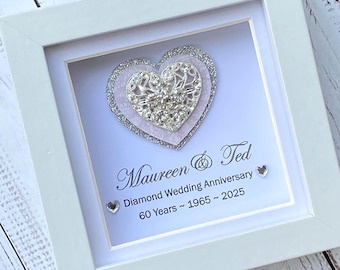 Op de afbeelding: Een witte schaduwdooslijst met een gelaagde hartversiering van zilveren glitter, lichtroze kant en een centraal zilveren filigraanhart met heldere kristallen. De tekst luidt: Maureen & Ted, Diamond Wedding Anniversary, 60 Years ~ 1965 ~ 2025.