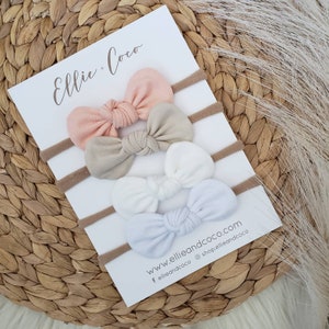 May include: Set of three fabric headbands with bows in peach, beige and white. The headbands are on a white card with the text "Ellie + Coco" and "www.ellieandcoco.com f ellieandcoco @shopellieandcoco".