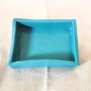 May include: A small, rectangular ceramic dish with a turquoise blue glaze. The dish has slightly rounded edges and a smooth, glossy finish.