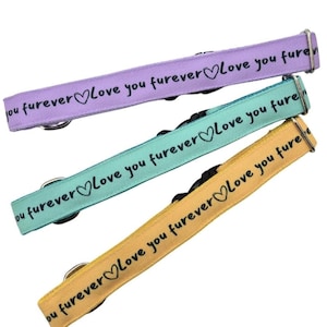 Puede incluir: Tres collares para mascotas en colores pastel: lavanda, turquesa y amarillo. Cada collar tiene el texto "Love you furever" con un símbolo de corazón. Los collares tienen herrajes metálicos y hebillas de plástico negro.