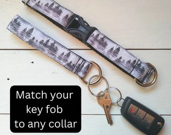 Puede incluir: Un llavero con estampado blanco y negro con un llavero plateado y una llave de coche negra. El llavero está unido a un collar de perro a juego con estampado blanco y negro. El texto "Match your key fob to any collar" está escrito en negro sobre fondo blanco.
