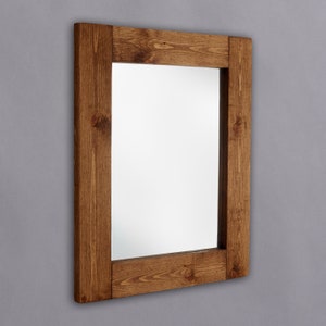 May include: A square wooden mirror with a brown stained frame. The frame is made of thick planks of wood.