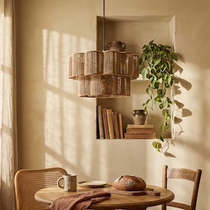 May include: A tiered pendant light fixture constructed from vertical tan rope segments. The cylindrical shade features two distinct levels of wrapped cord, suspended by a thin black rod from the ceiling above a wooden dining table.