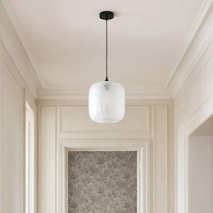 May include: A pendant light fixture featuring a rounded, textured white glass shade suspended from a thin black cord and a matching black circular ceiling canopy. The glass has a subtle, uneven surface finish that diffuses light evenly.