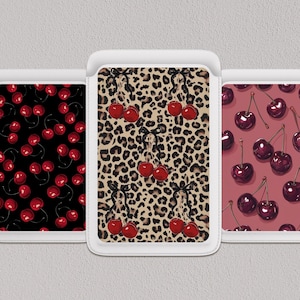 May include: Three phone cases with cherry designs. One case has a black background with red cherries, another has a leopard print background with cherries, and the third has a maroon background with cherries.