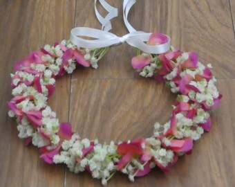 May include: A white ribbon tied around a pink and white flower crown. The crown is made of small white flowers and pink rose petals.